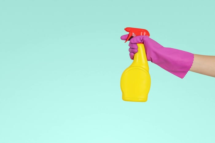 A person holding a yellow spray bottle with blue background