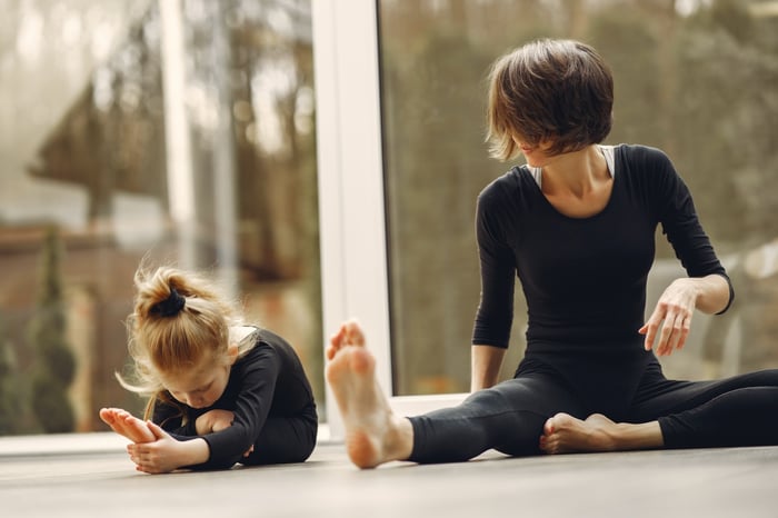 Unrecognizable Female trainer teaching girl doing forward fold yoga