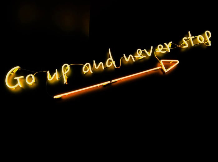 Go up and Never stop yellow neon letters sign arrow pointing up on black background