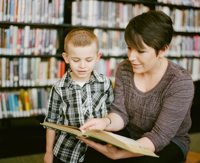 Kobieta z książką w ręku ucząca małe dziecko.
