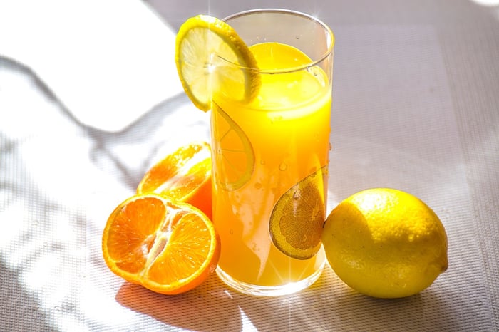 copo de suco de laranja ao lado de um limão e uma laranja cortada