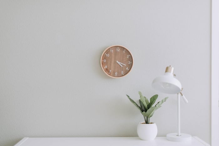 Un reloj de pared sobre una mesa con una lámpara y una planta