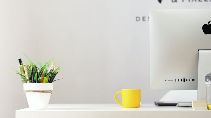 A white desk with a computer, a yellow mug and a plant on it