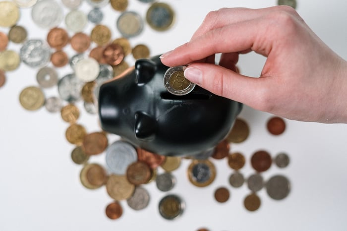 A black piggybank being filled with more coins, viewed from above