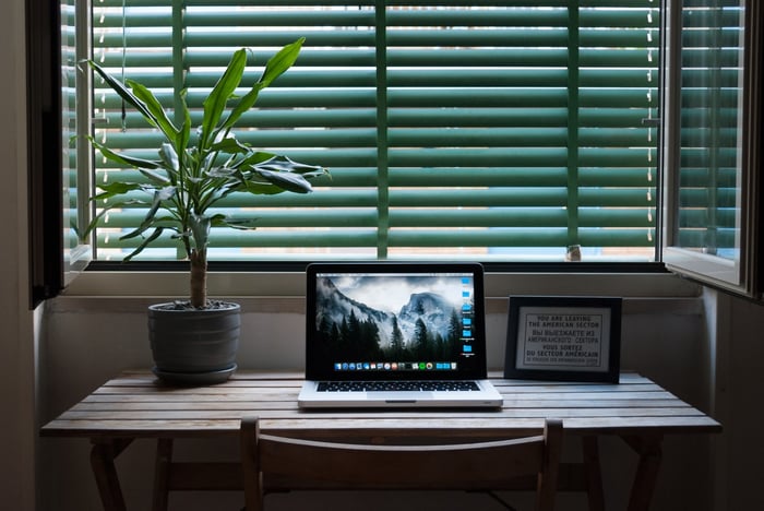 Una computadora portátil en un escritorio junto a una ventana y una planta en maceta