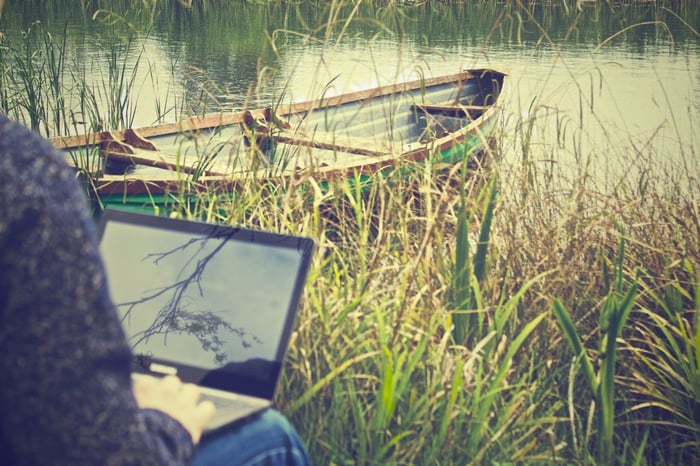 person sitting by a lake typing on a laptop
