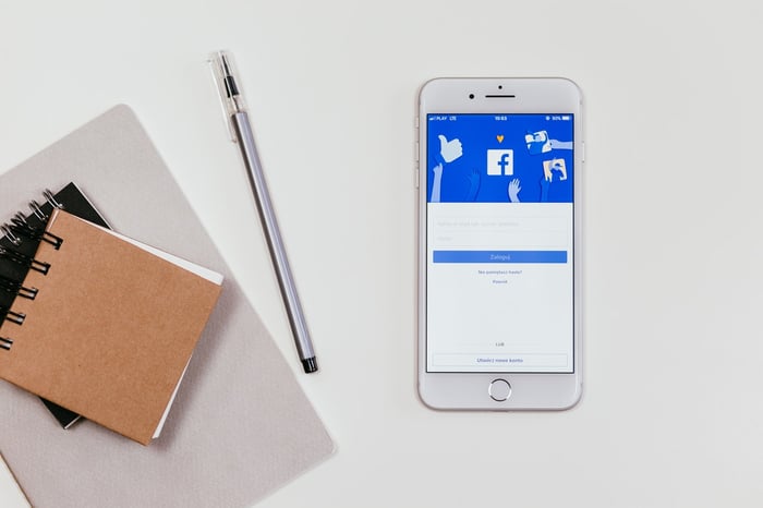 Facebook open on a mobile phone with pens and stationery on a white table