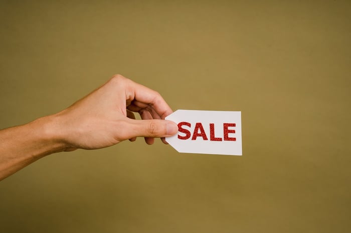 Person holding a sale tag against a mustard background