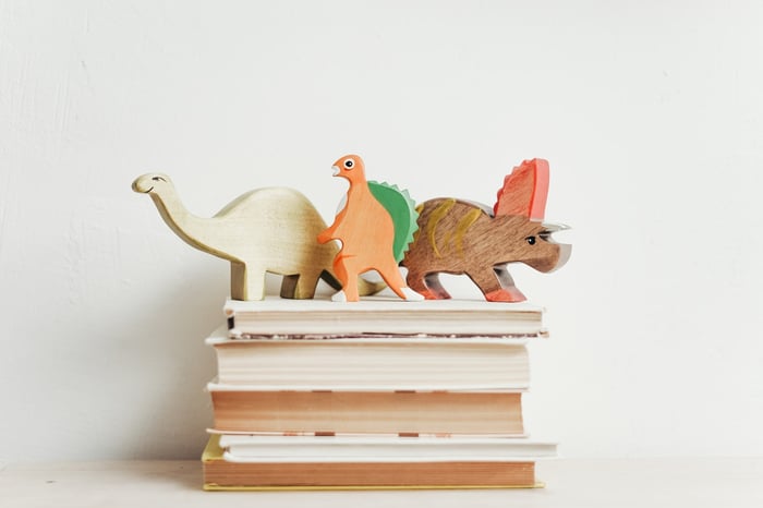 Wooden dinos on a pile of books against a white background