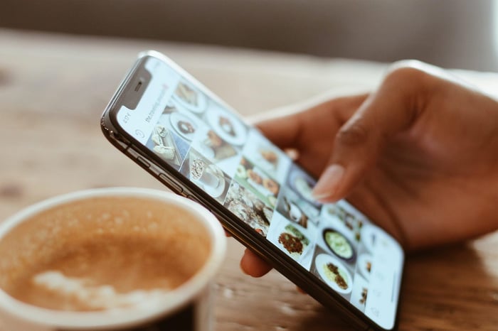 person scrolling instagram on phone with cup of coffee on table