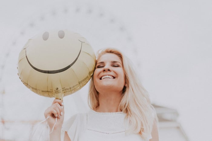 woman holding smiling emoji balloon and laughing
