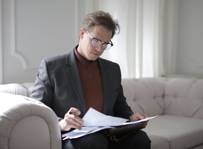 Un homme dans une suite qui lit des documents sur un canapé blanc.
