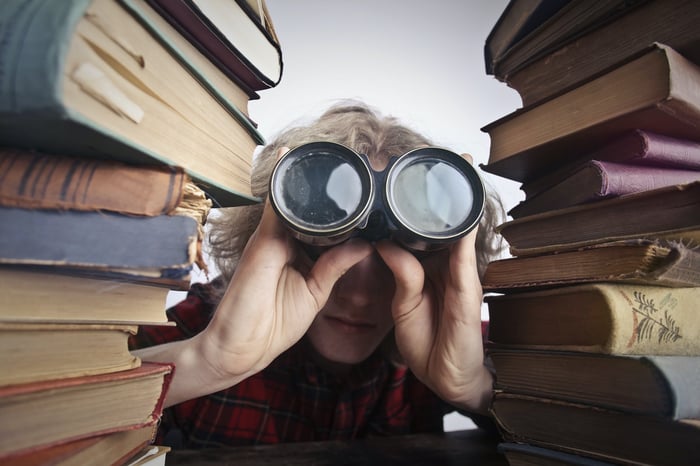 A man with binoculars in between two piles of books