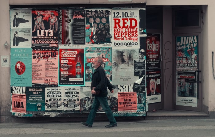 A person walking on a sidewalk past a wall of ads 