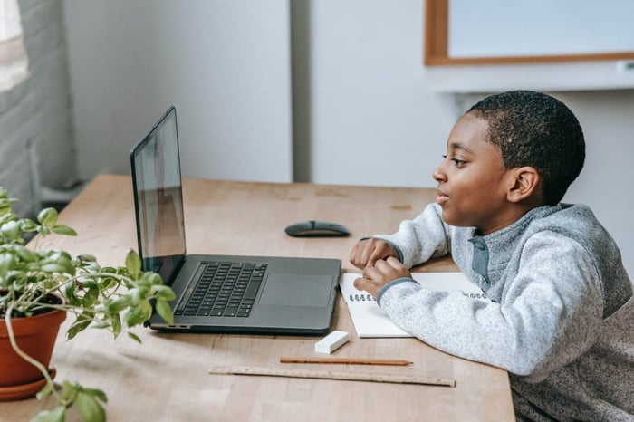 ujęcie z boku chłopca siedzącego przed laptopem przy biurku