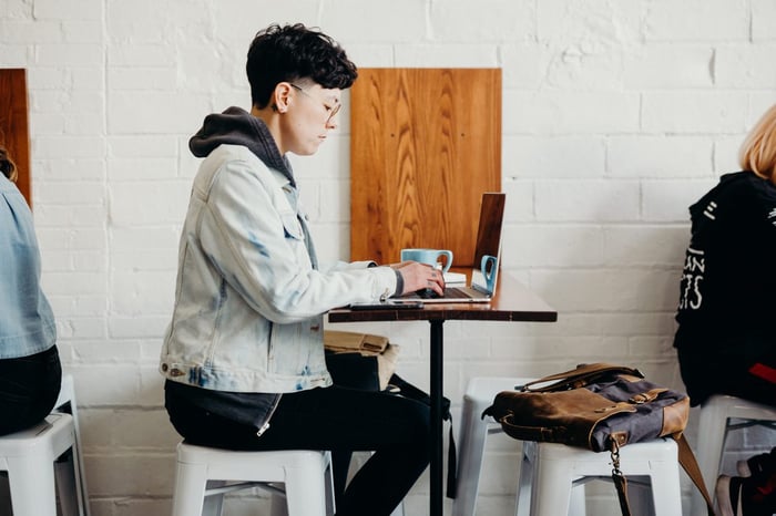 side shot of person sitting on stool in cafe with a laptop