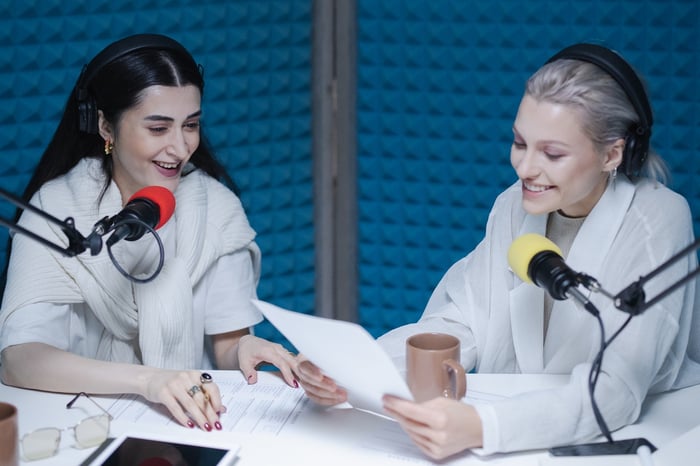 Two women recording a podcast in a room with a blue wall