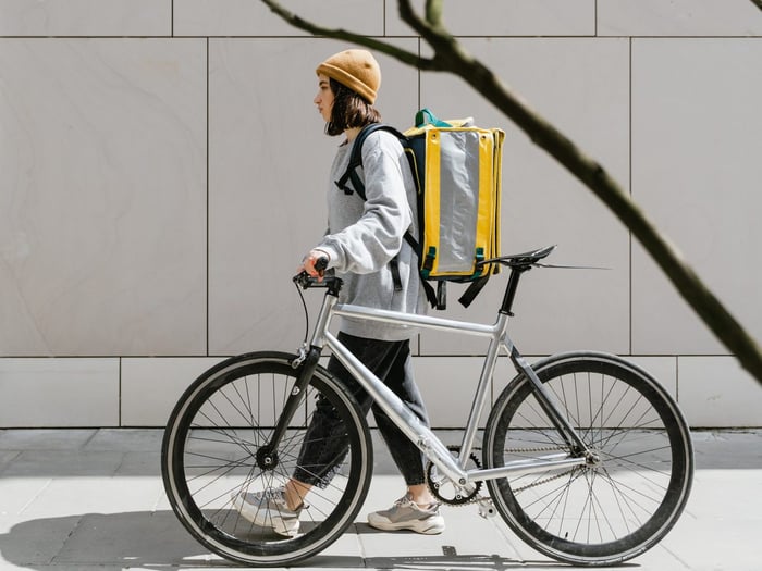 kobieta prowadząca rower i niosąca torbę kurierską