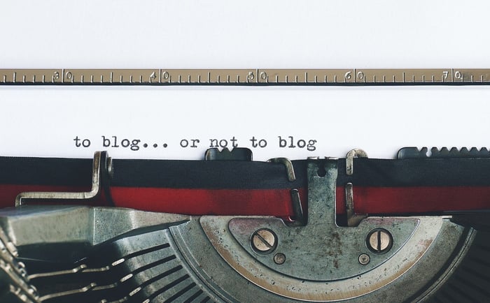 Vieille machine à écrire avec "to blog or not to blog" écrit sur un papier.
