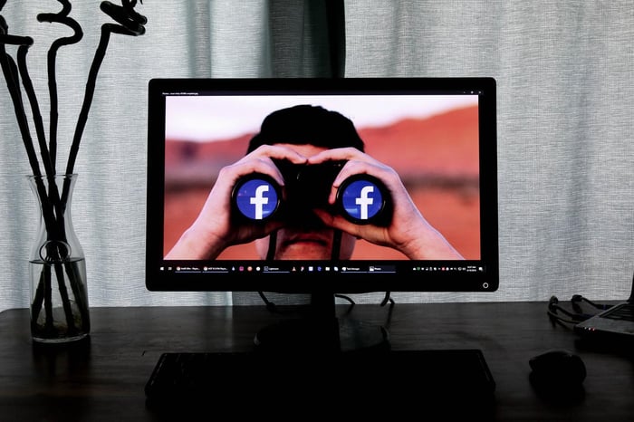 monitor de computador exibindo homem usando binóculos com o símbolo do facebook sobre as lentes