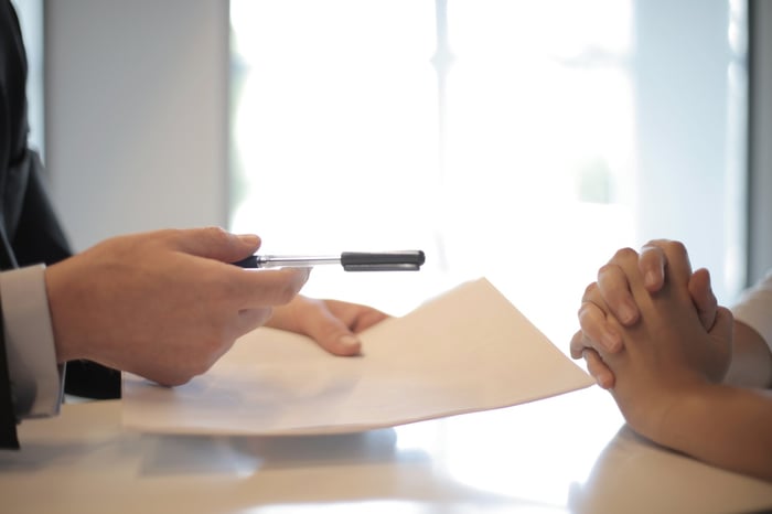 A person handing another person a pen while holding papers 