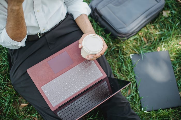 Person outside with a takeaway coffee cup and their laptop in their lap 