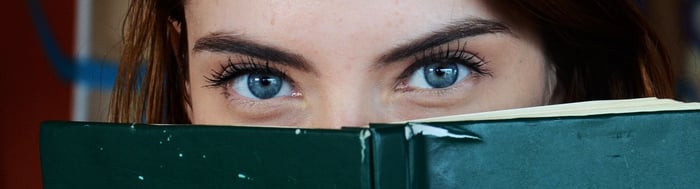 Woman peering behind a book with big eyes