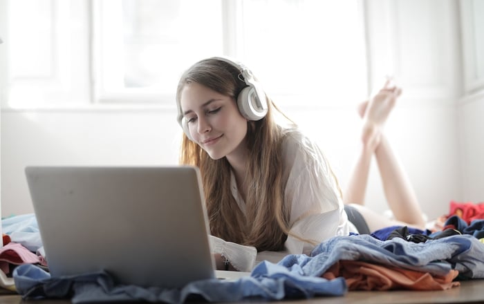 Una ragazza sdraiata che ascolta musica o un podcast con le cuffie e un laptop davanti