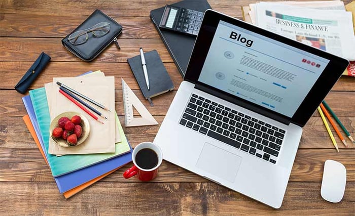 Un laptop con la scritta "blog" sullo schermo, libri e oggetti vari sul tavolo