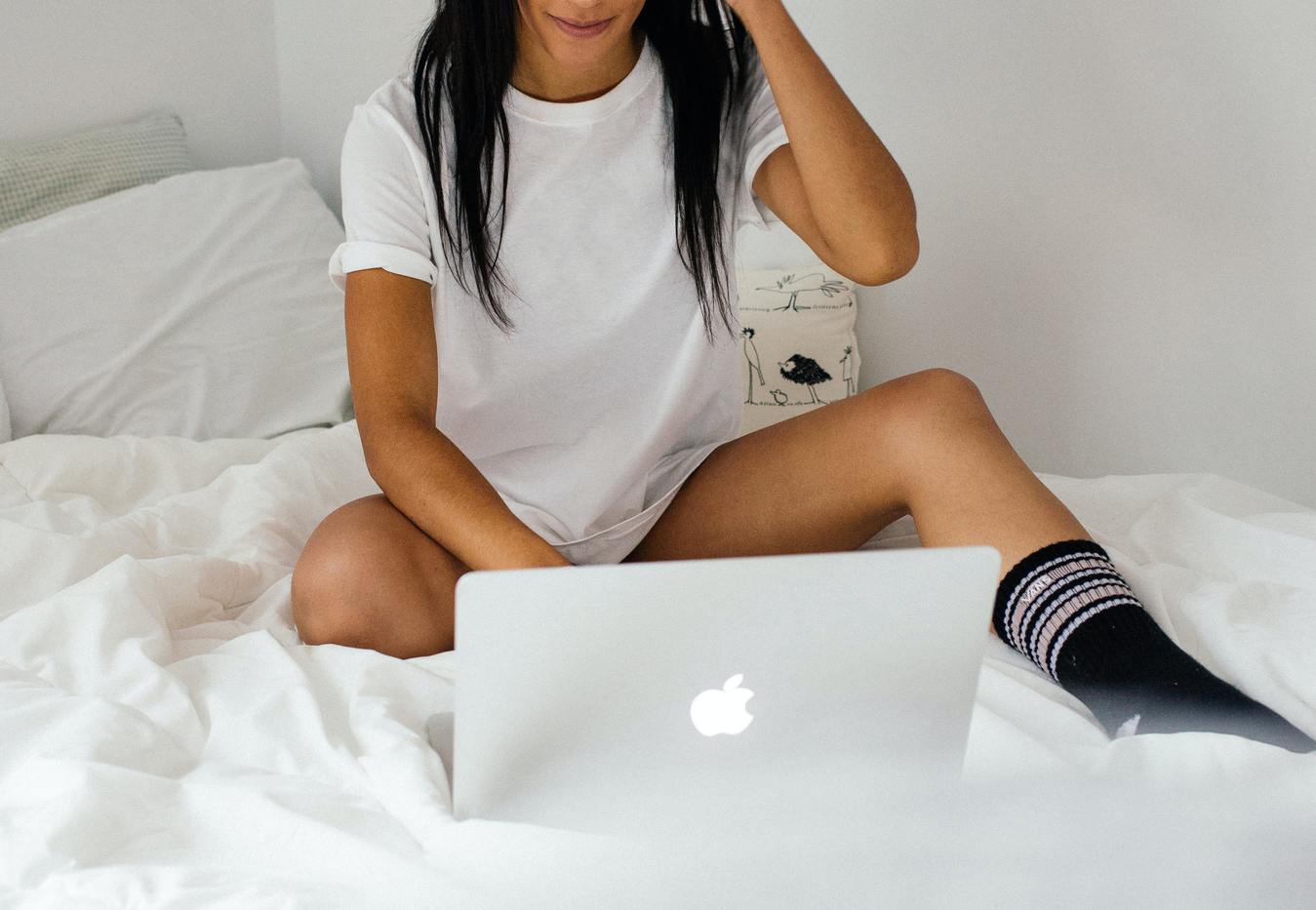 Wanita duduk di atas kasur sedang menggunakan laptop