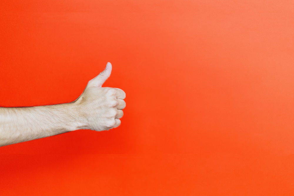 person's hand holding thumb up against orange background